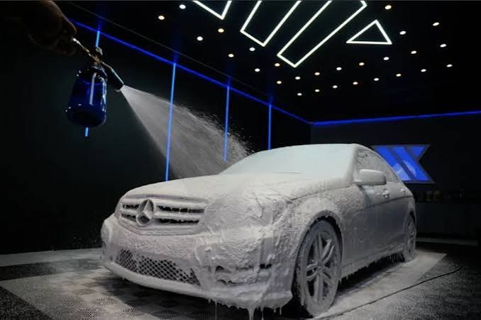 Sedan coberto de espuma ativa em uma garagem de estética automotiva com luzes azuis